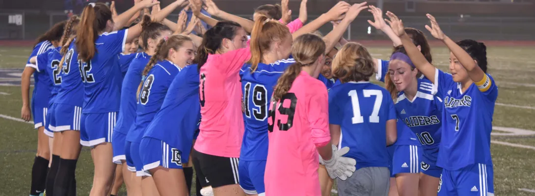 High school girls soccer team celebrating with their arms up and their coach walking in between them