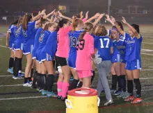 High school girls soccer team celebrating with their arms up and their coach walking in between them